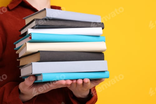 Preview: Woman holding stack of different books on yellow background, closeup. Space for text