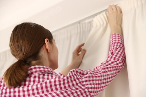Preview: Woman hanging up window curtains at home, low angle view