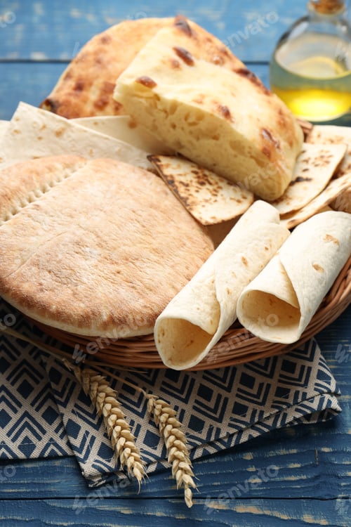 Preview: Tasty pita bread and lavash in wicker basket on blue wooden table, closeup