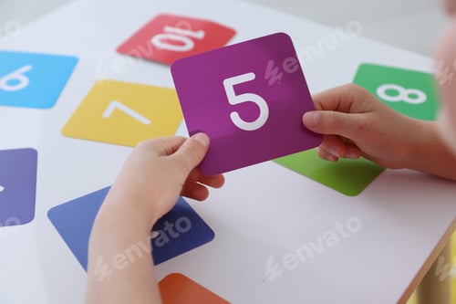 Preview: Little boy learning numbers with colorful cards at white table indoors, closeup