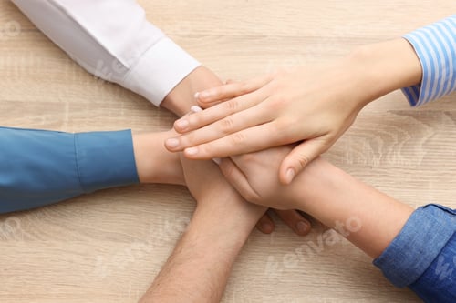 Preview: People holding hands together at wooden table, above view. Team building