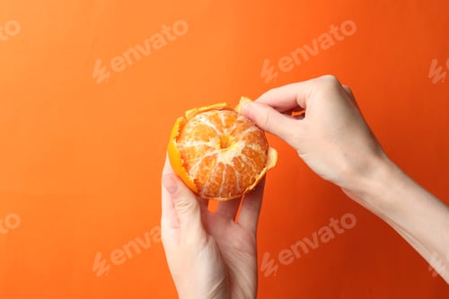 Preview: Woman peeling tangerine on orange background, closeup