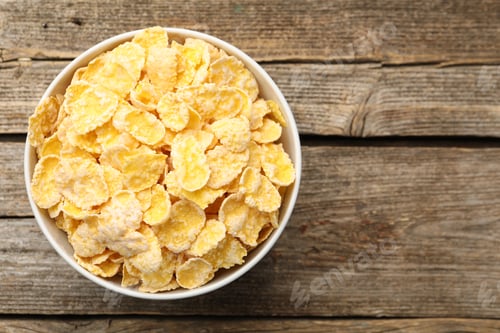 Preview: Tasty corn flakes in bowl on wooden table, top view. Space for text