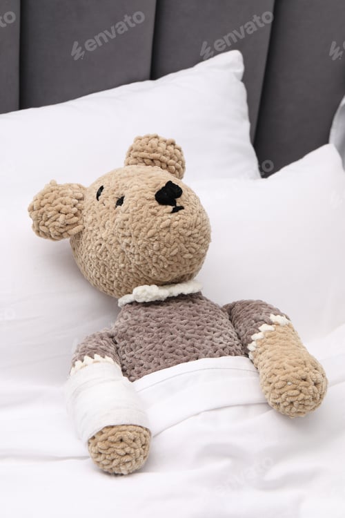 Preview: Toy cute bear with bandage under blanket in bed