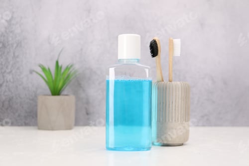Preview: Bottle of mouthwash and toothbrushes on white table in bathroom