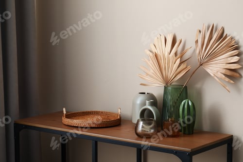Preview: Beautiful vases and other decor on wooden table near beige wall indoors
