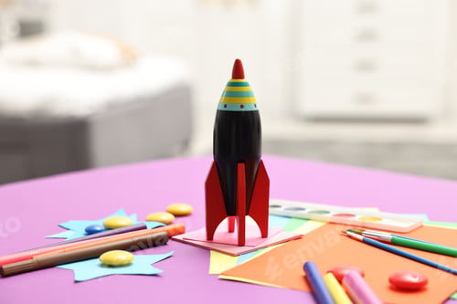 Preview: Toy rocket and art materials on purple table indoors, closeup. Space for text