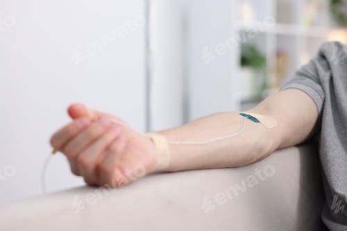 Preview: Man with IV drip on sofa at home, closeup