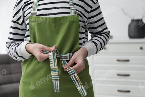 Preview: Woman tying clean apron at home, closeup