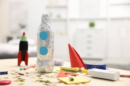 Preview: Handmade rockets and art materials on table indoors. Space for text