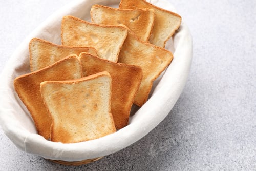 Preview: Slices of tasty toasted bread in basket on light grey table, closeup