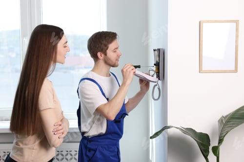 Preview: Man installing modern intercom system and woman indoors