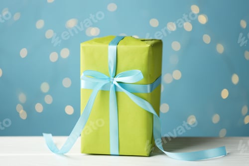 Preview: One beautiful gift box on white wooden table against light blue background with blurred lights, clos