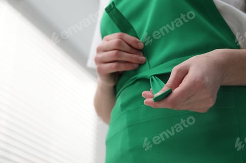 Preview: Woman tying clean apron at home, closeup. Space for text