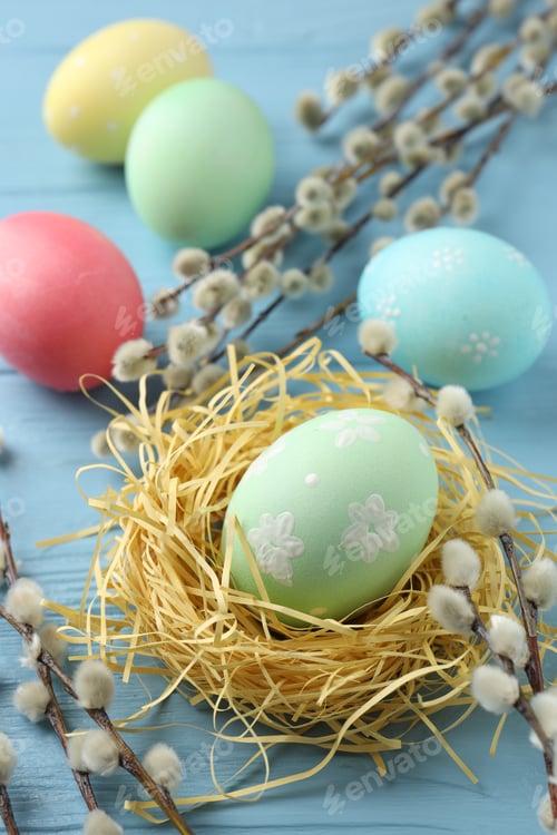Preview: Painted Easter eggs, nest and willow branches on light blue wooden table, closeup