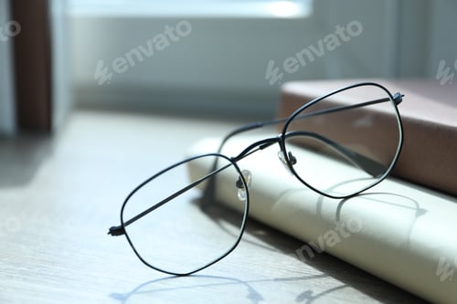 Preview: Stylish glasses and books on wooden table near window indoors, closeup