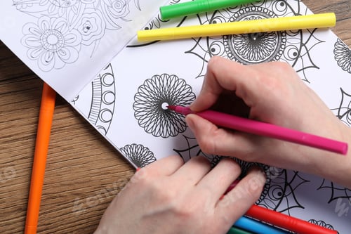 Preview: Woman coloring antistress picture with felt tip pen at wooden table, top view