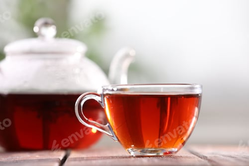 Preview: Aromatic tea in glass cup and teapot on table against blurred background, closeup
