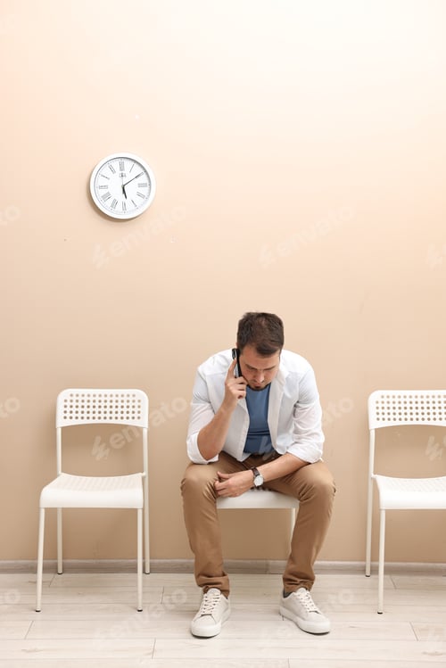Preview: Man talking on smartphone and waiting for appointment indoors
