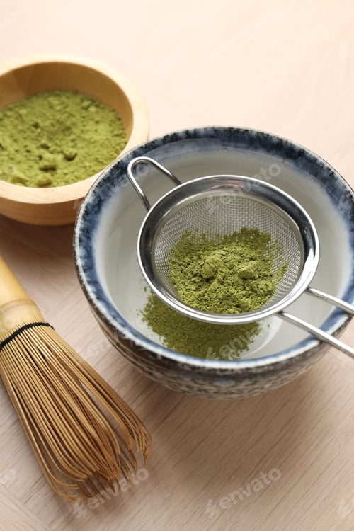 Preview: Sifting matcha powder into bowl and bamboo whisk on wooden table, closeup