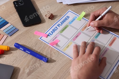 Preview: Man using yearly planner at wooden desk, closeup