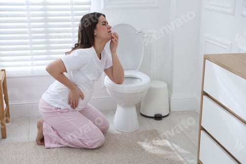 Preview: Pregnant woman suffering from nausea near toilet bowl in bathroom. Toxicosis during pregnancy