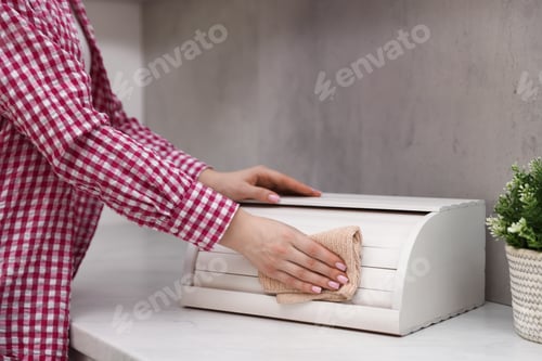 Preview: Woman wiping dust from breadbox at white marble countertop in kitchen, closeup
