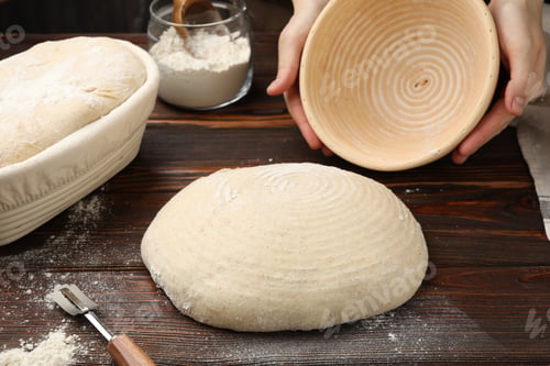 Preview: Woman taking sourdough out of proofing basket at wooden table, closeup