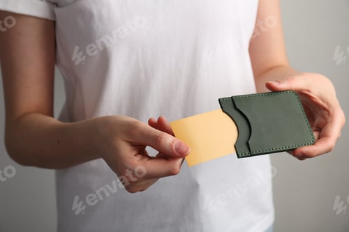 Preview: Woman holding leather business card holder with card on grey background, closeup