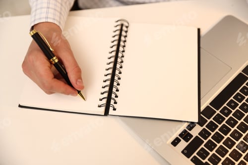 Preview: Man writing in notebook with pen at white desk, above view