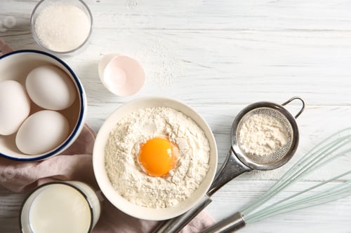 Preview: Flour with yolk in bowl and other ingredients for dough on white wooden table, flat lay