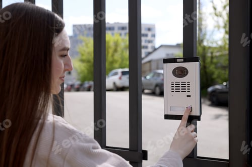 Preview: Woman pressing button on intercom panel outdoors