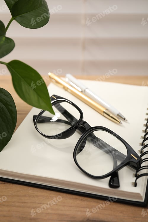 Preview: Pair of stylish glasses, notepad and pens on wooden table indoors, closeup