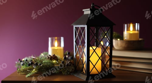 Preview: Christmas lantern, burning candles, books and decor on wooden table against dark pink background, cl