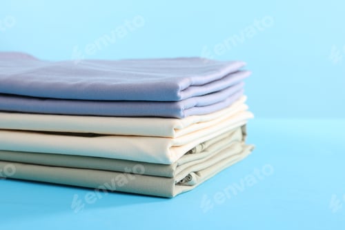 Preview: Stack of colorful bed linens on light blue background, closeup. Space for text