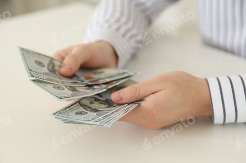 Preview: Man counting dollar banknotes at white table, closeup