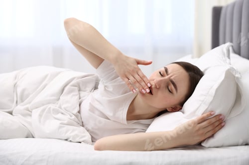 Preview: Young woman lying on soft pillow and yawning in bed at home