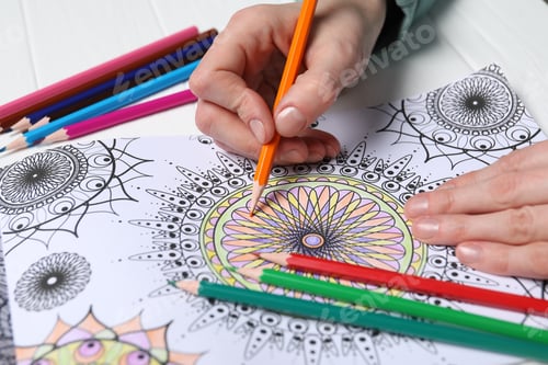 Preview: Woman coloring antistress picture with pencils at white table, closeup