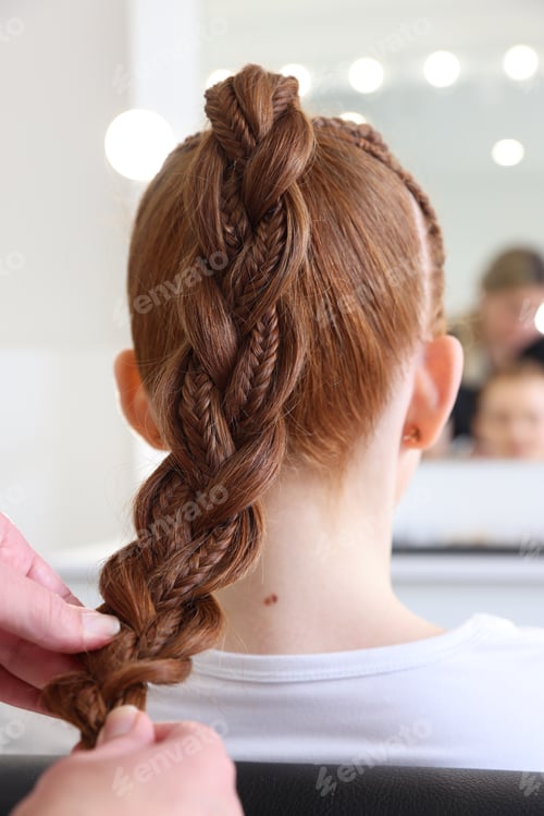 Preview: Hairstylist braiding teenage girl's hair in salon, closeup
