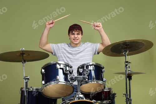 Preview: Smiling teenage boy in baseball cap with drumsticks learning how to play drums on green background