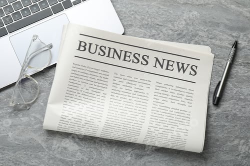 Preview: Newspaper, laptop, glasses and pen on grey desk, flat lay