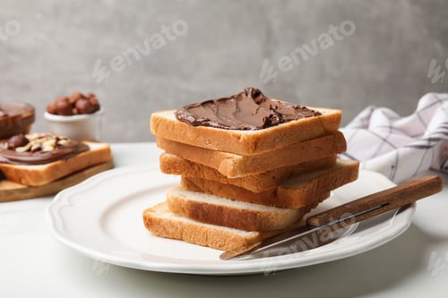 Preview: Toasts with chocolate paste, hazelnuts and knife on white table, closeup