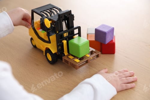 Preview: Little girl with toy forklift and colorful cubes at wooden table, closeup