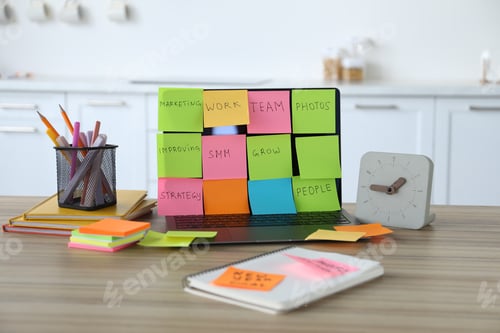Preview: Laptop with colorful sticky notes, stationery and alarm clock on wooden table indoors. Multitasking,