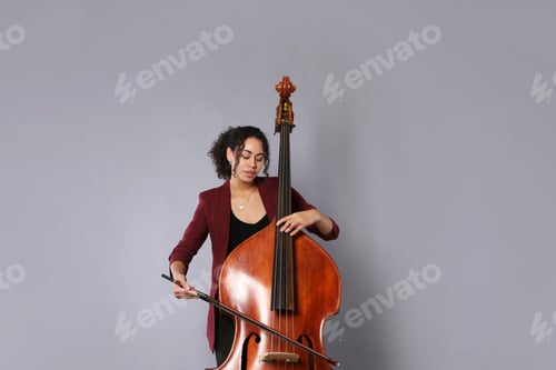 Preview: Woman playing double bass on grey background, low angle view