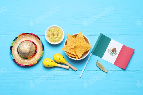 Preview: Mexican flag, sombrero hat, maracas, nachos chips and guacamole on light blue wooden table, flat lay