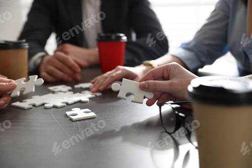 Preview: Team building. Group of businesspeople with takeaway cups solving puzzle together at dark wooden tab