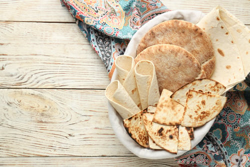 Preview: Pita bread and lavash in basket on wooden table, top view. Space for text
