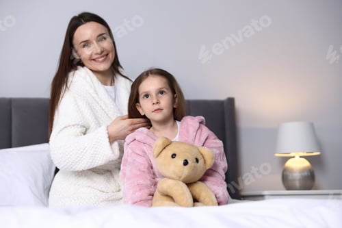 Preview: Mother brushing her daughter's hair on bed at home