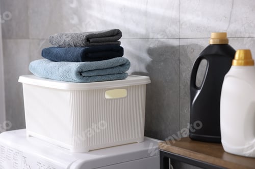 Preview: Many clean towels in laundry basket on washing machine and detergents indoors, closeup